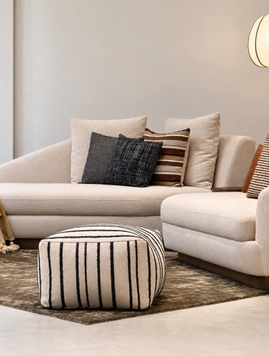 Black and cream striped pouf by NicChris styled in a modern living room with a curved cream sofa, wooden lounge chair, and olive green rug