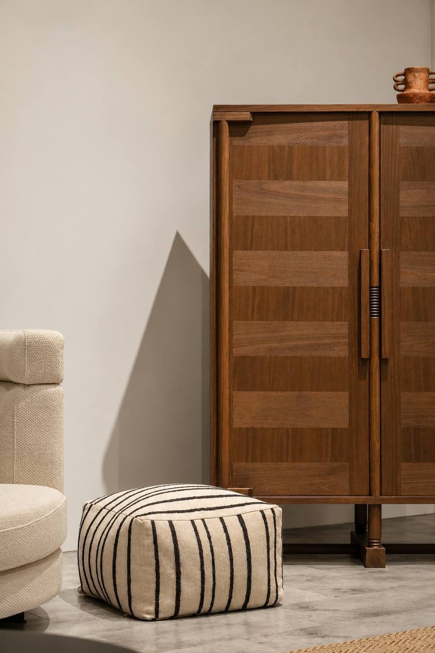 Black and cream striped upholstered pouf by NicChris, styled beside a cream sofa and wooden cabinet in a warm modern living room